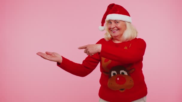 Großmutter im Weihnachtsmann-Pullover zeigt Daumen hoch und zeigt auf leeren Platz, Werbefläche — Stockvideo