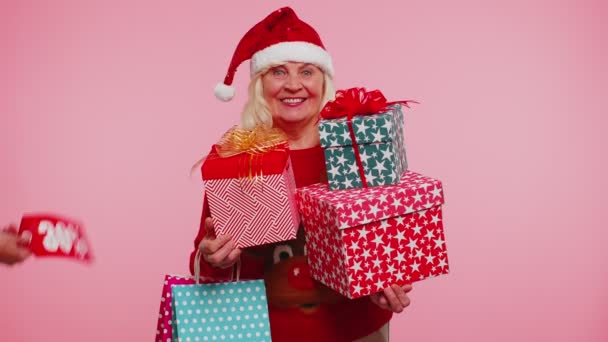 Бабуся похилого віку тримає подарункові коробки і отримує різдвяні знижки на написи банерні тексти — стокове відео