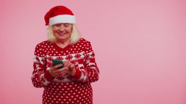 Büyükanne Noel süveteri ve cep telefonu boş yeri gösteriyor, reklam alanı.