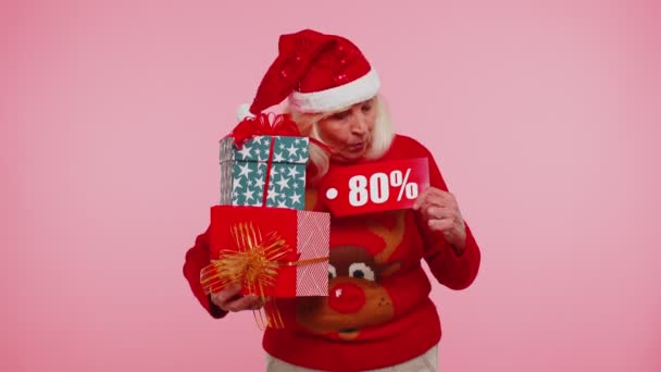 Babička ve vánočním svetru ukazuje dárkové krabice a 80 Procento sleva nápisy banner text — Stock video