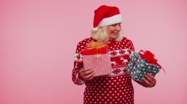 Noel Baba süveteri giymiş büyük anne bir Noel hediyesi kutusunu sunuyor, ellerini kameraya uzatıyor.