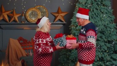 Romantik son sınıf çifti Noel ağacını süslemek için birbirlerine hediye kutuları sunuyorlar.