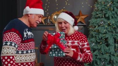 Dedem sürpriz büyükanneme Noel hediyesi veriyor. Şapkalı mutlu yaşlı çift.