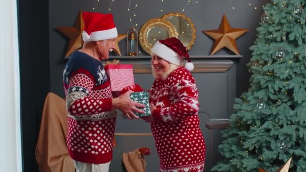 Romántica pareja de ancianos presentándose cajas de regalo en casa cerca de decorar el árbol de Navidad — Vídeos de Stock