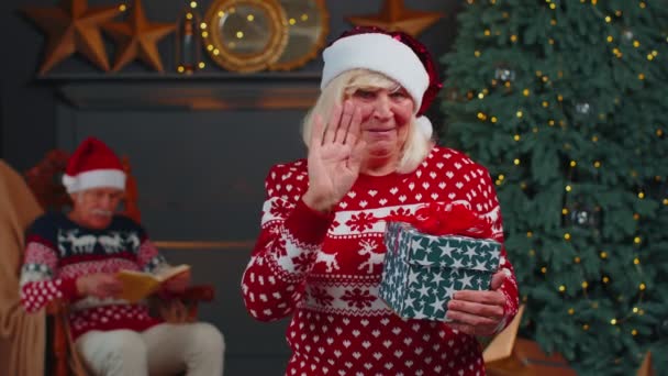 Avó sênior em camisola de Natal sorrindo amigável para a câmera e acenando mãos gesticulando Olá — Vídeo de Stock