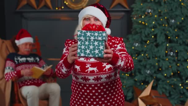 원문 기사보기 할머니가 새해 스웨터를 입고 모자를 쓰고 크리스마스 선물 상자를 선물하는 모습, 집에서 휴일을 보내는 모습 — 비디오