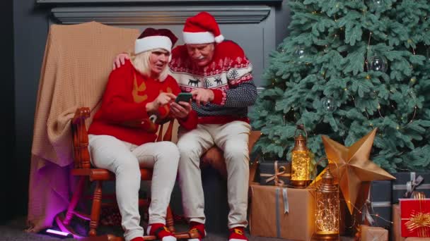 Senior család pár keres vásárlás online karácsonyi ajándékok mobiltelefon alkalmazás otthon — Stock videók