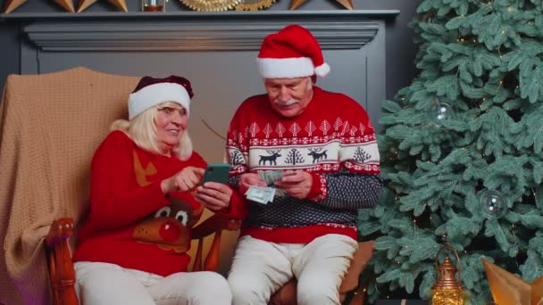 Senior famille couple recherche achat en ligne cadeaux de Noël dans l'application de téléphone mobile à la maison — Video