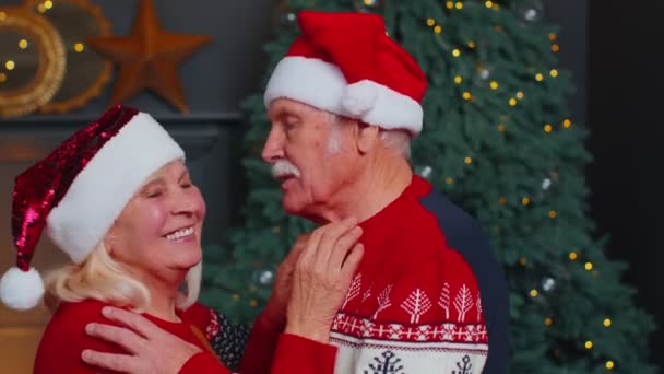 Senior couple family in Santa Claus hats celebrating Christmas looking at camera and hugging at home — Stock Video