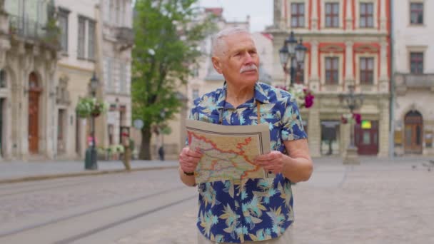 Starszy stylowy turysta dziadek człowiek spacery ulicą szuka drogi przy użyciu papierowej mapy w mieście — Wideo stockowe
