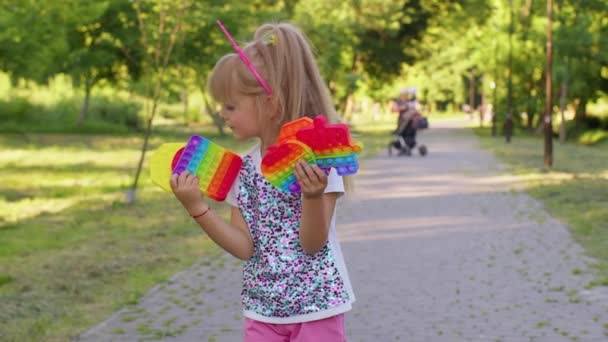 Дитяча дівчинка, яка тримає стискаючий антистресовий сенсорний екран, штовхає популярну іграшку в громадському парку — стокове відео