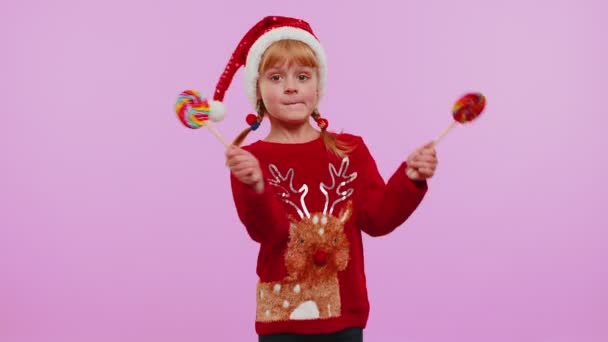 Chica alegre en jersey de Navidad, sombrero sosteniendo caramelos a rayas piruletas, bailando, haciendo caras tontas — Vídeos de Stock