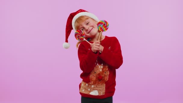 Funny girl in New Year sweater holding candy striped lollipops hiding behind them, fooling around — Stock Video