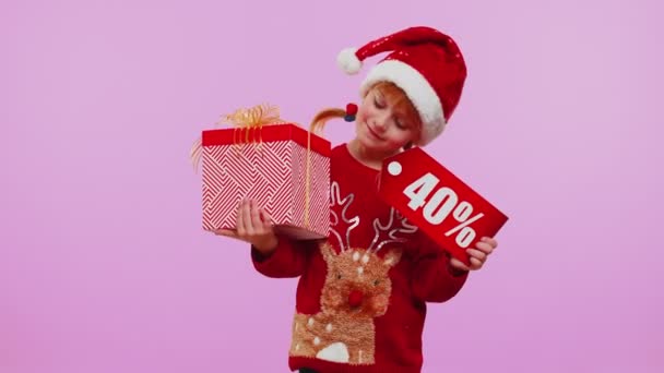 Νήπιο κορίτσι στο καπέλο Χριστούγεννα δείχνει κουτί δώρου και 40 τοις εκατό έκπτωση επιγραφές banner σημείωμα κείμενο — Αρχείο Βίντεο
