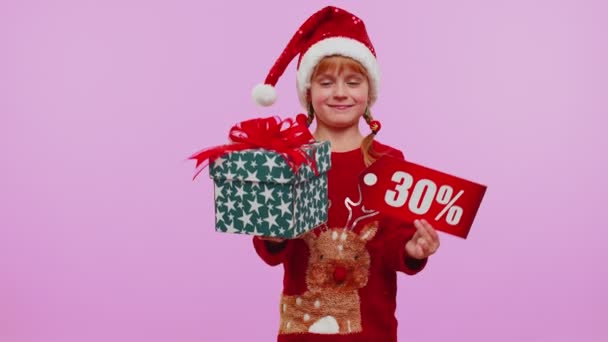 Νήπιο κορίτσι στο καπέλο Χριστούγεννα δείχνει κουτιά δώρων και 30 τοις εκατό έκπτωση επιγραφές banner κείμενο — Αρχείο Βίντεο
