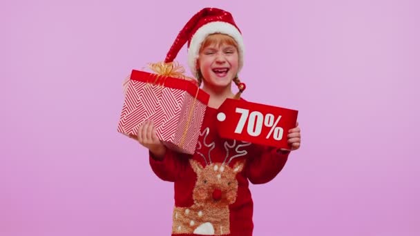 Girl kid in red Christmas hat showing gift box and 70 Procent discount inscriptions banner text note — Stock video