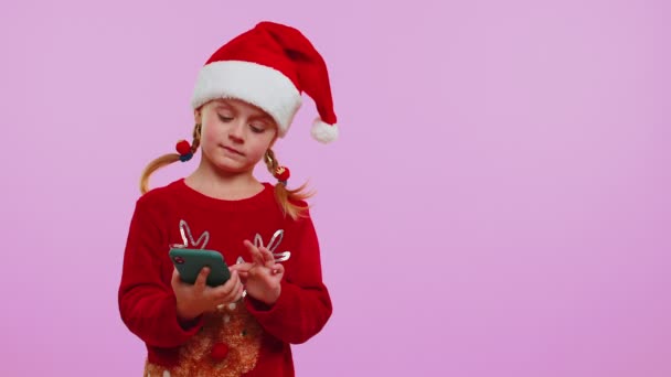 Κορίτσι νήπιο σε Χριστούγεννα Σάντα καπέλο με κινητό τηλέφωνο δείχνει κενό μέρος, περιοχή διαφήμισης — Αρχείο Βίντεο