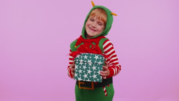 Chica alegre en suéter de Santa presentar una caja de regalo de Navidad, extiende sus manos a la cámara — Vídeo de stock