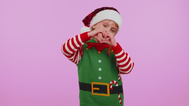 Noel Elf kostümlü gülümseyen kız kalp hareketi yapıyor. Aşk işareti duygularını ifade ediyor. — Stok video