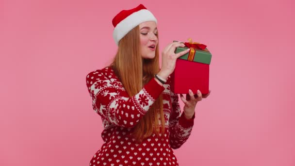 有趣的女孩穿着新年毛衣，鹿角收到礼物，对里面的礼品盒感兴趣 — 图库视频影像