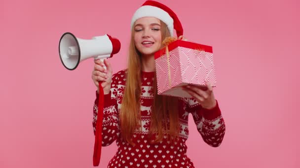 Дівчина в різдвяному светрі з подарунковою коробкою кричить в мегафоні оголошує про знижки продажу покупки — стокове відео