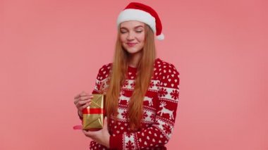 Noel Baba şapkalı neşeli kız bir Noel kutusunu sunuyor, bayram hediyesiyle heyecanlanıyor.