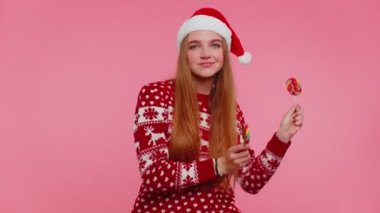 Noel süveteri giymiş neşeli bir kız, elinde şeker çizgili lolipoplar, dans eden, aptal suratlar yapan bir şapka.