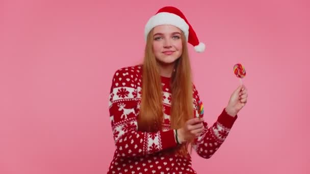 Joyful girl in Christmas sweater, hat holding candy striped lollipops, dancing, making silly faces — Stock Video