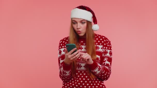 Felnőtt lány karácsonyi pulóver keres smartphone kijelző őszintén örvendezve nyerj sikert szerencsét — Stock videók