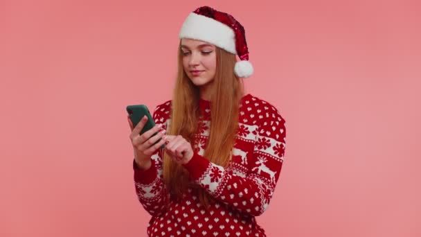 Девушка в рождественском свитере Санта делает звонок с мобильного телефона, чтобы поздравить друзей семьи — стоковое видео
