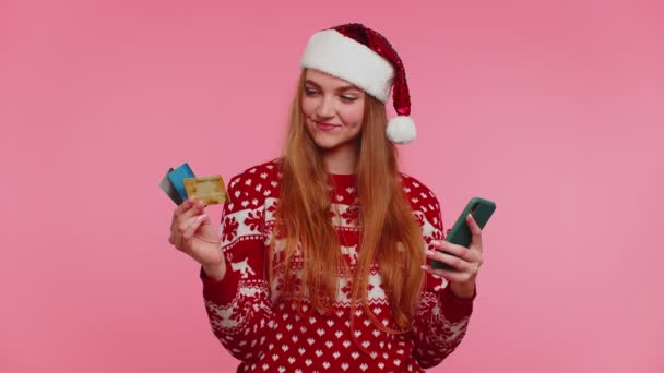 Mujer en jersey de Navidad utilizar el teléfono celular móvil y tarjeta bancaria de crédito de plástico, ganar, calebrar, guau — Vídeos de Stock