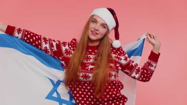 Взрослая девушка-патриот в рождественском свитере размахивает и заворачивает в израильский национальный флаг, празднуя — стоковое видео