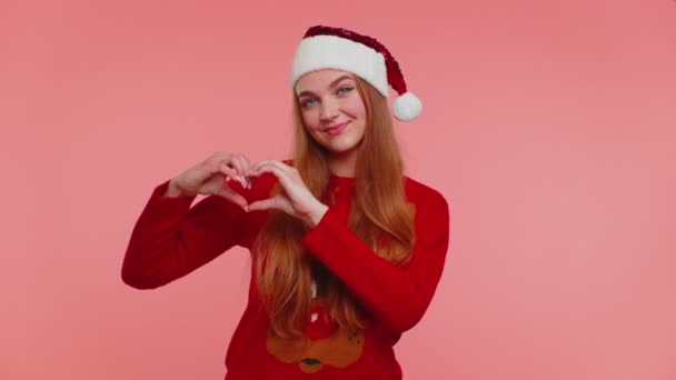 Smiling girl in Christmas sweater makes heart gesture demonstrates love sign expresses good feelings — Stock Video