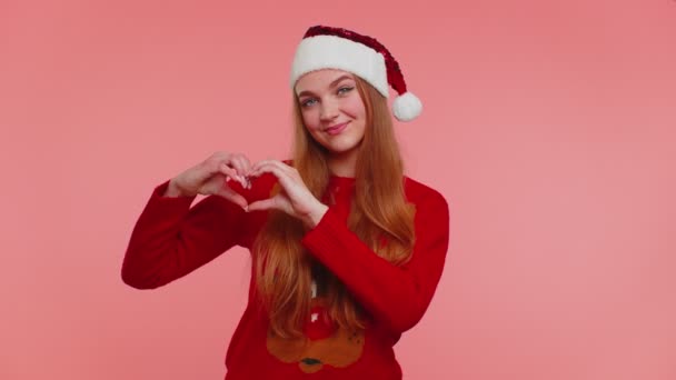 Glimlachend meisje in kerst trui maakt hart gebaar toont liefde teken drukt goede gevoelens — Stockvideo