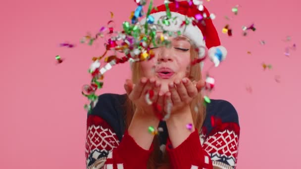 Vidám mosolygós lány karácsonyi Mikulás pulcsi fúj arany csillogó konfetti felé kamera — Stock videók