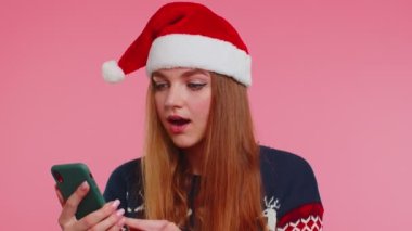 Şık bir Noel kazağı giyen, akıllı telefon görünümlü, neşeli, başarılı bir zafer kazanan kadın.