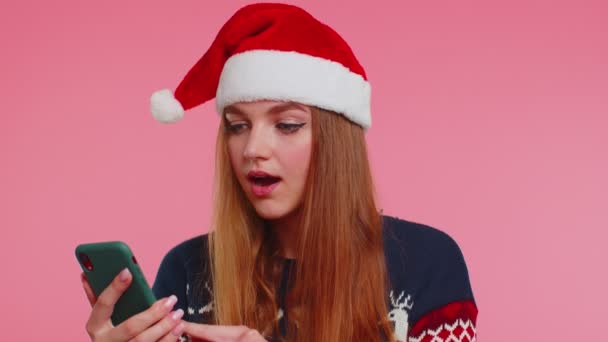 穿着时髦圣诞毛衣的女人看起来很像智能手机显示出诚挚的喜悦赢得了成功 — 图库视频影像