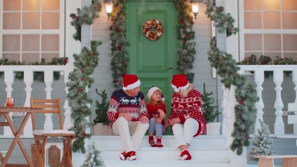 Abuelos mayores cerca de la casa de Navidad decorada celebrando junto con la nieta en casa — Vídeos de Stock