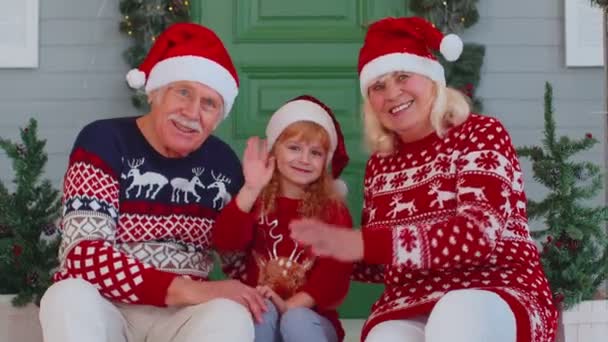 Senior old couple grandparents with grandchild girl kid waves hand hello, hi near Christmas house — Stock Video