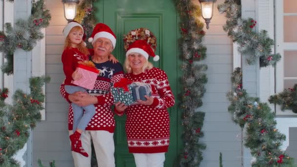 Gelukkig senior grootouders met kleindochter houden veel geschenkdozen in de buurt van het huis van Kerstmis, vieren — Stockvideo