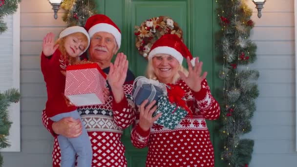 Старший дедушка бабушки с внучкой, стоящей на крыльце рождественского дома, машет привет — стоковое видео