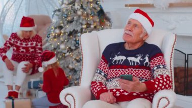 Yaşlı büyükbaba Noel hediyesi alıyor. Evde akıllı telefondan alışveriş yapıyor.