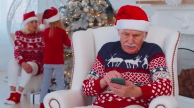 Yaşlı büyükbaba Noel hediyesi alıyor. Evde cep telefonuyla alışveriş yapıyor.