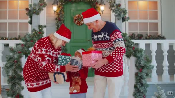 Senior grandparents with grandchild girl kid exhcanging gifts near Christmas house celebrating Xmas — Stock Video