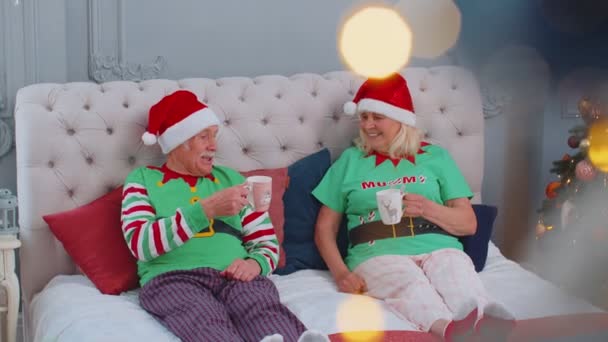 Starsza para dziadków pije gorącą herbatę na łóżku z wnuczką maluchem, świąteczny poranek — Wideo stockowe