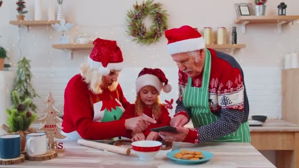 Oudere grootouders en kleinkind kijken kooklessen met digitale tablet in de kerstkeuken — Stockvideo