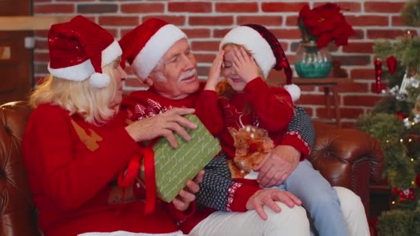 Abuelos regalando la caja de regalo de Navidad a la nieta feliz sorprendida en casa, celebrando — Vídeo de stock