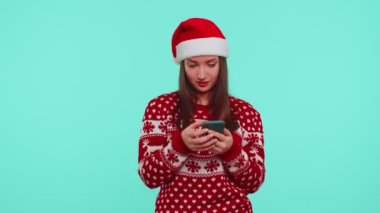 Noel süveteri giyen yetişkin bir genç kız. Akıllı telefon görüntüsü. Sevinçten havalara uçuyor.