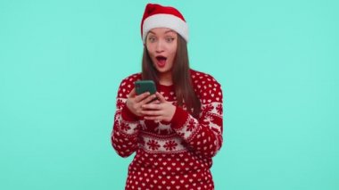 Noel süveteri giyen genç kız akıllı telefon görüntüsü veriyor. İçtenlikle seviniyor. Başarılı olma şansı.