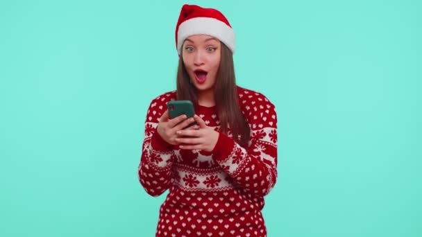 Noel süveteri giyen genç kız akıllı telefon görüntüsü veriyor. İçtenlikle seviniyor. Başarılı olma şansı. — Stok video